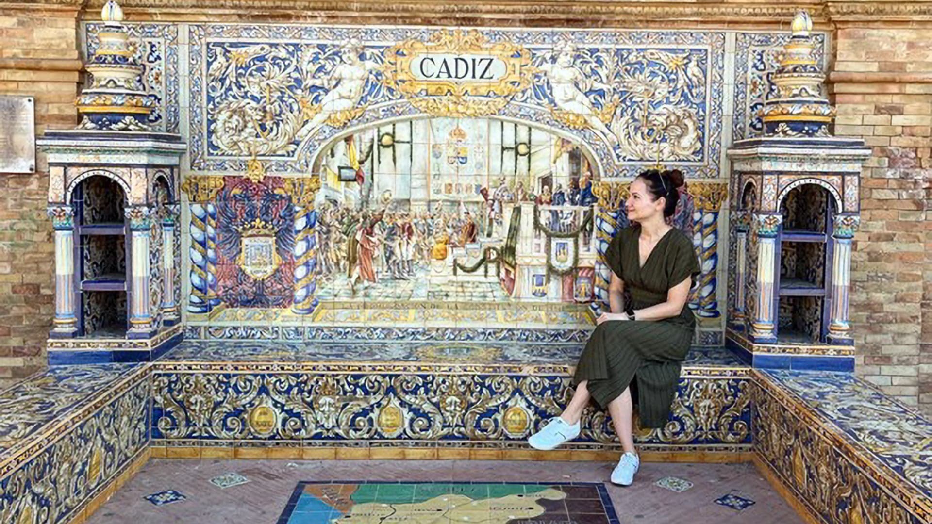 Loredana Gogoescu of Destguides seated in front of a vibrant tiled wall in Cadiz.
