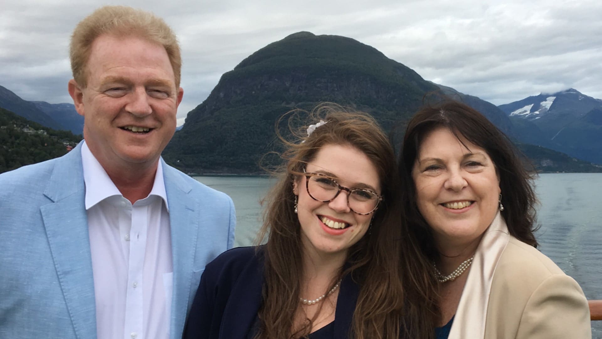 Dr Elizabeth McNaught and her parents Nick and Carol Pollard, of Family Mental Wealth, posing for a picture in front of a lake and large mountain.