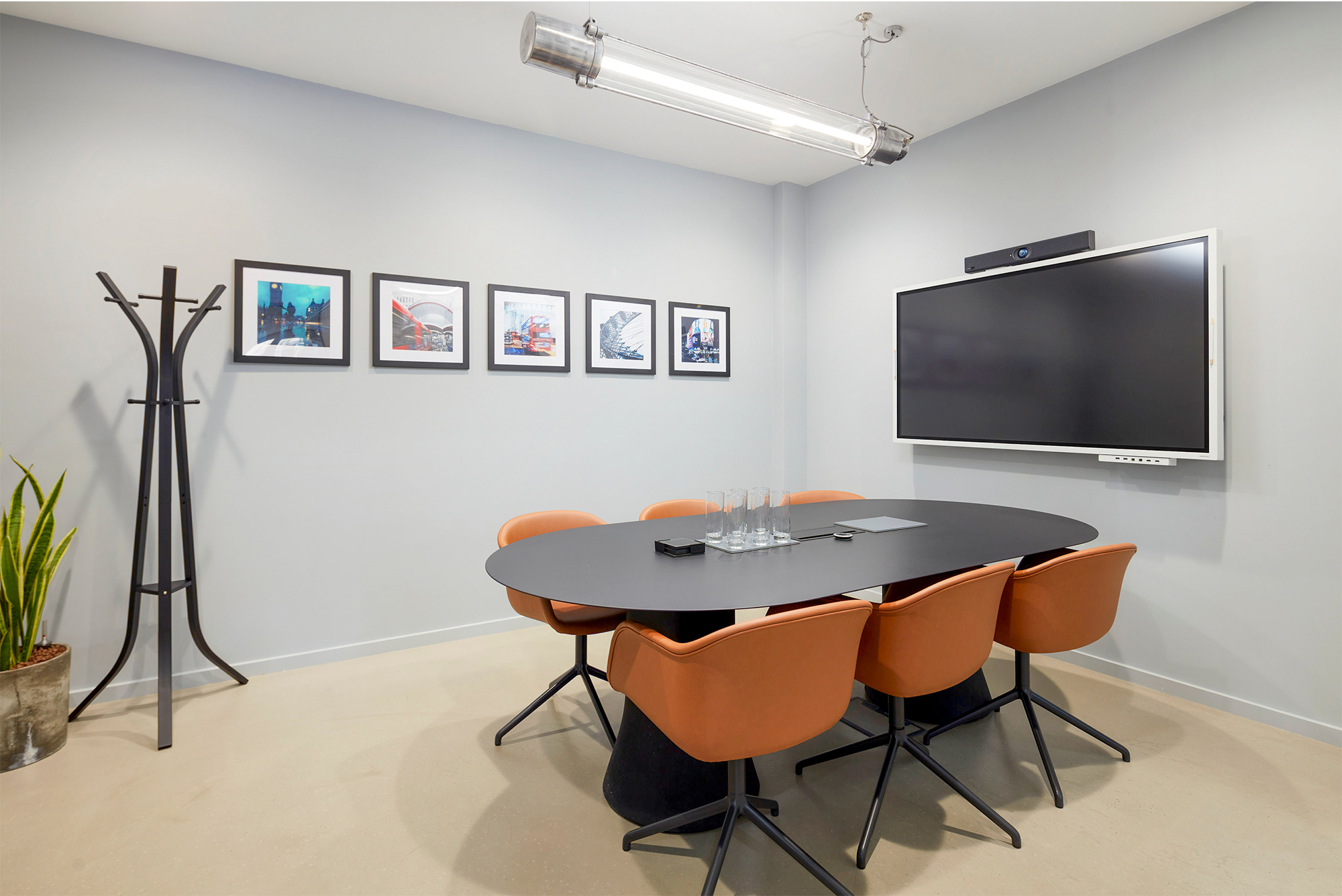 Meeting room with black table and 6 brown leather chairs. Large display screen and framed photographs on walls.