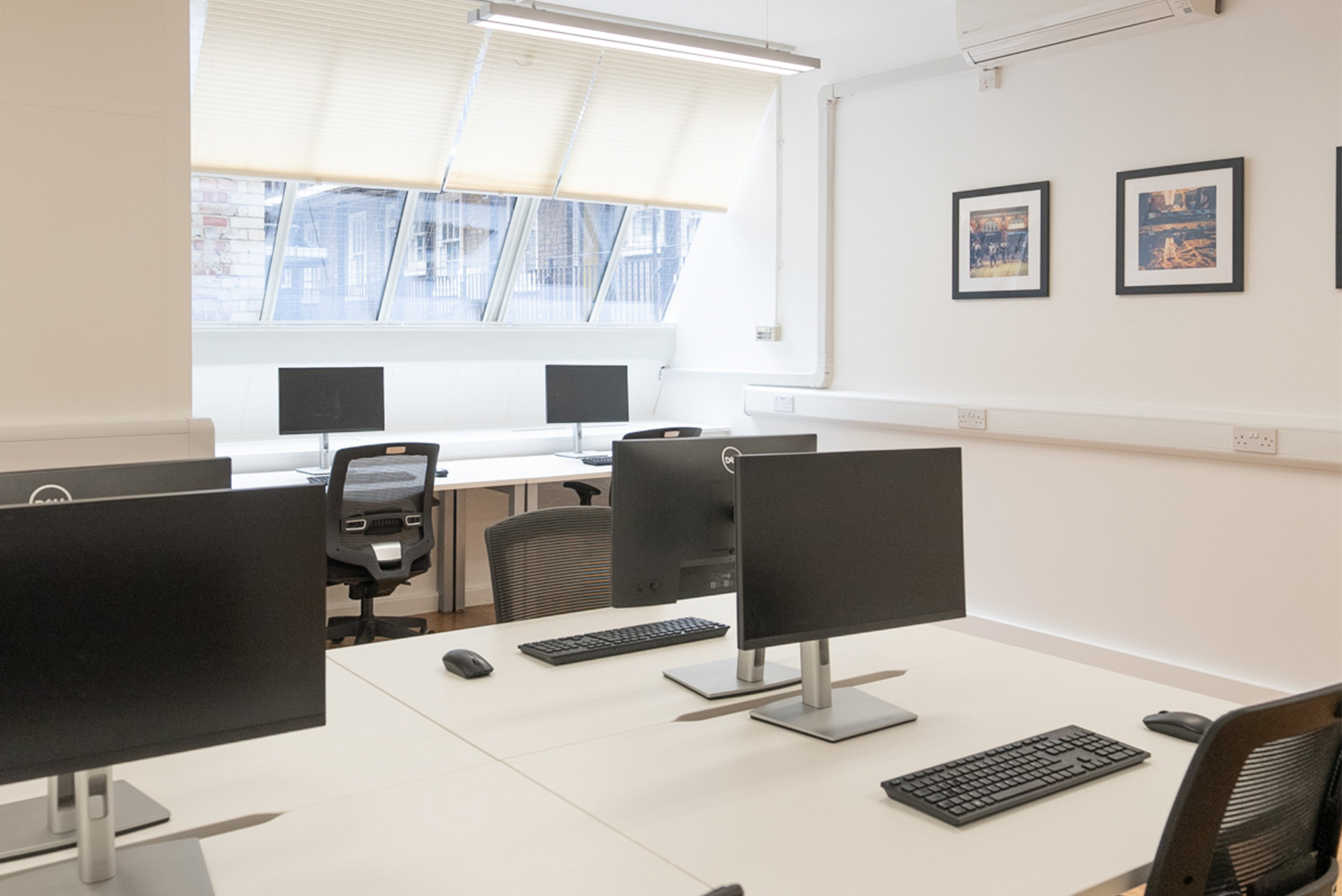 Serviced office with white desks, black operator chairs and windows with silver venetian blinds.