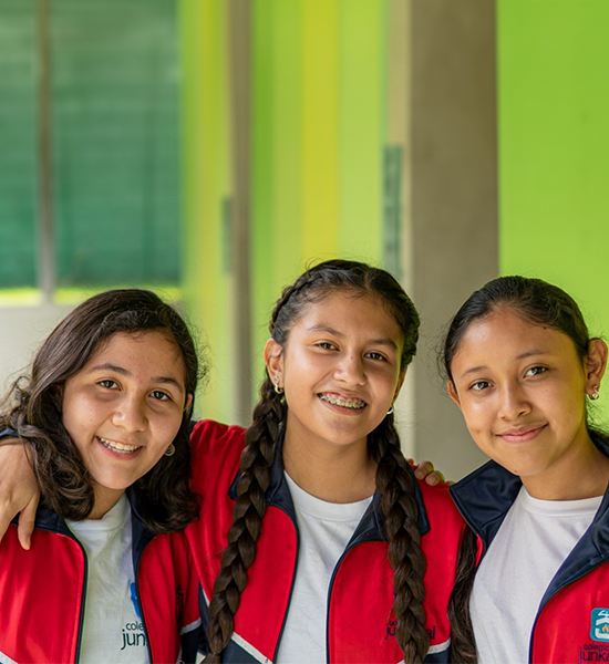 Portrait of 3 schoolgirls from the Colegio Junkabal in Guatemala City, wearing white t-shirts, and red and black tracksuit jackets.