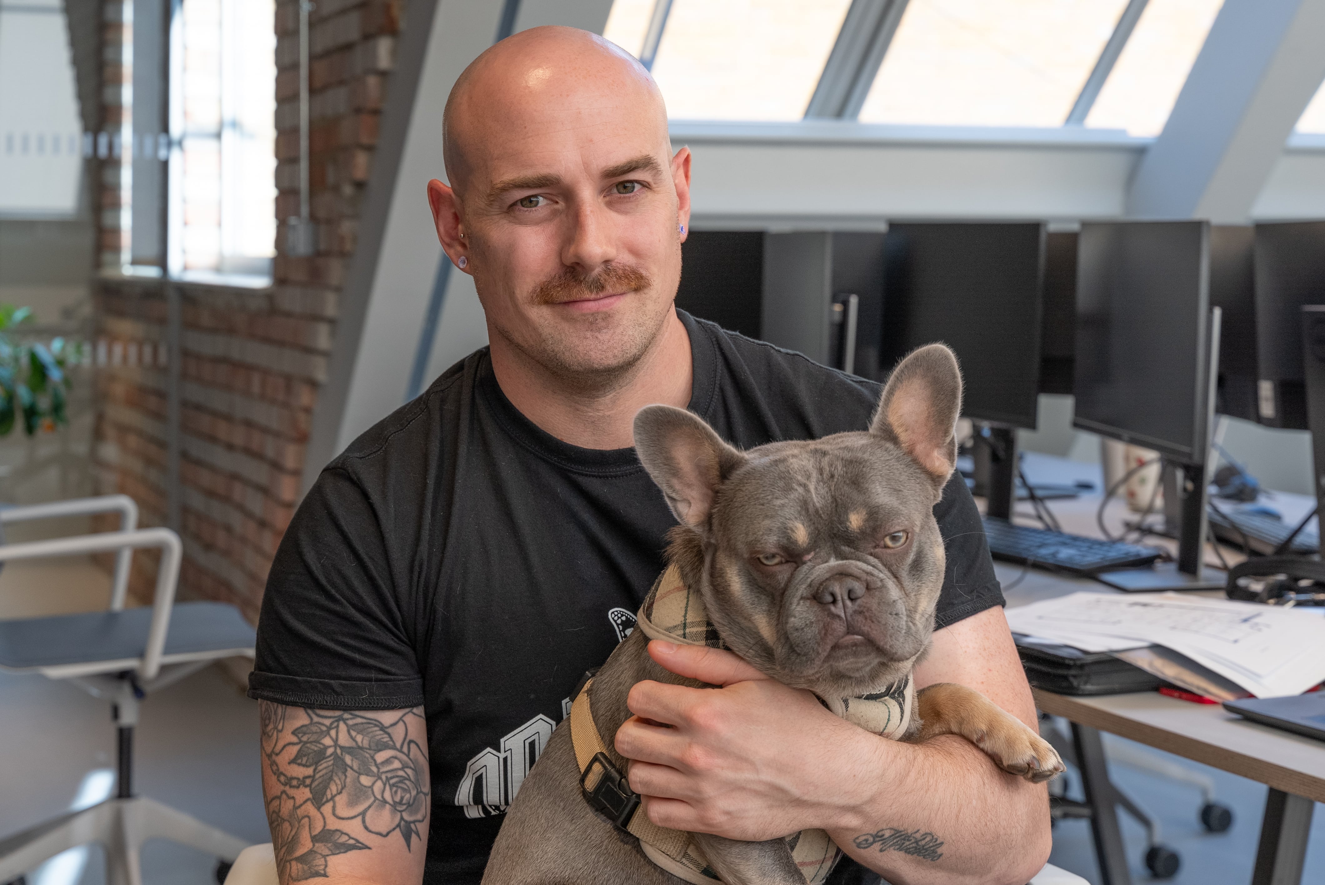 Liam, our Serviced Office Manager, smiling and sitting at his desk with his French Bulldog, Oscar, on his lap.