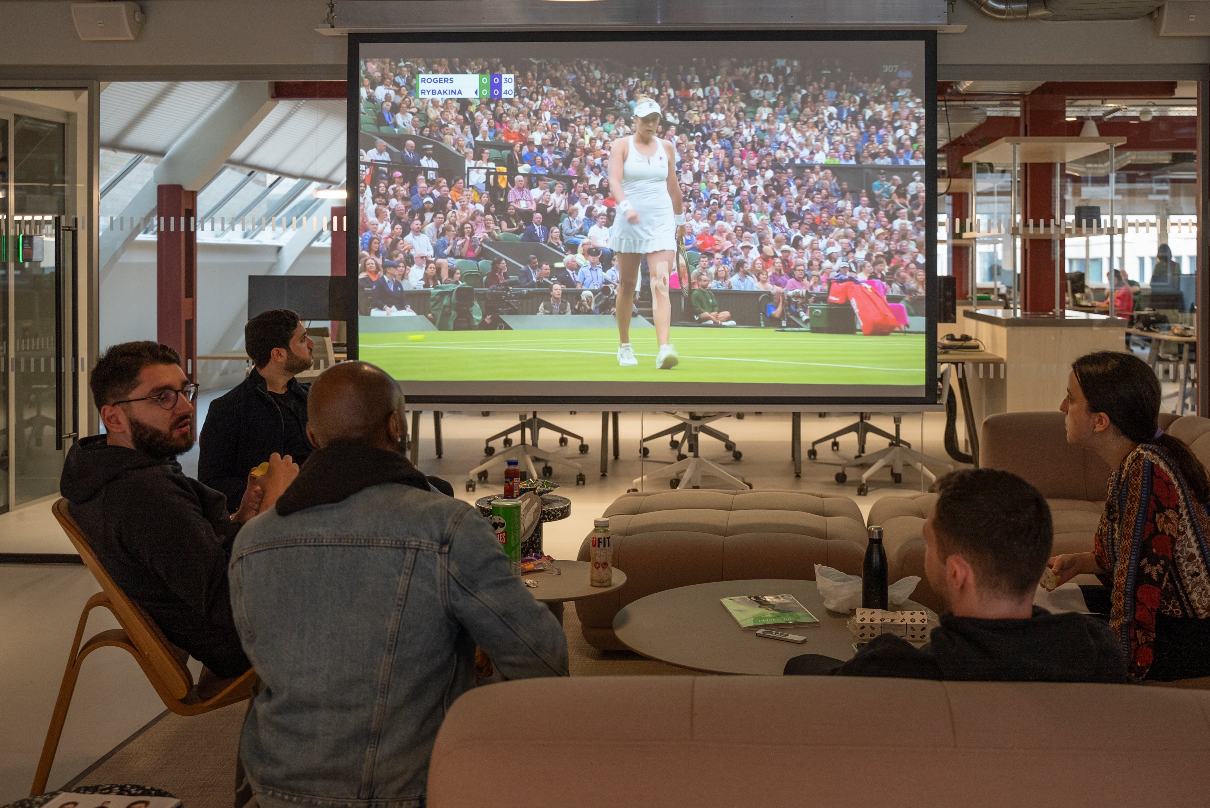 5 members of staff sitting in our social area, and watching tennis from Wimbledon on our large projector screen.