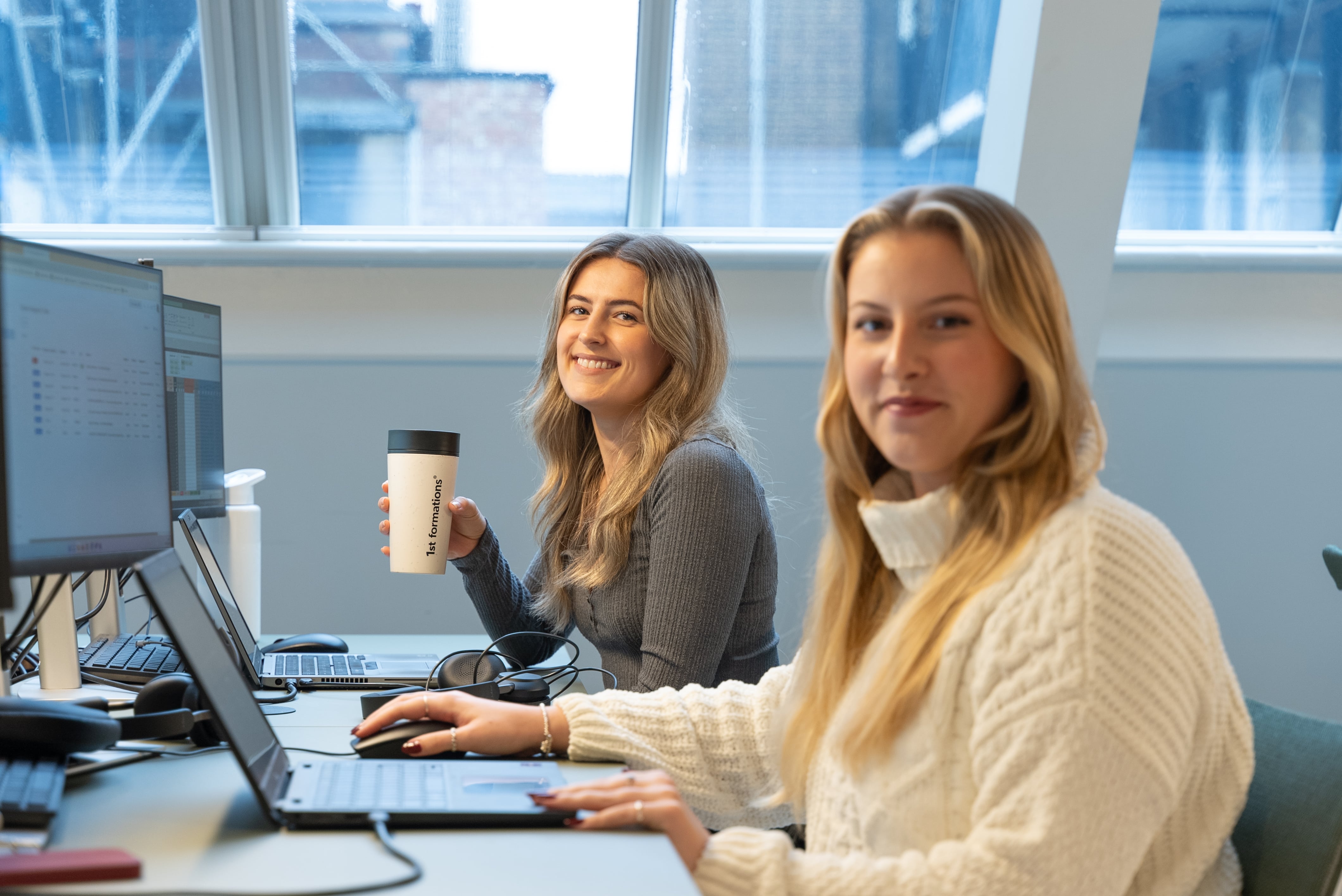 Hannah and Jodie, from our Customer Retention Team, smiling and sitting at their desks.